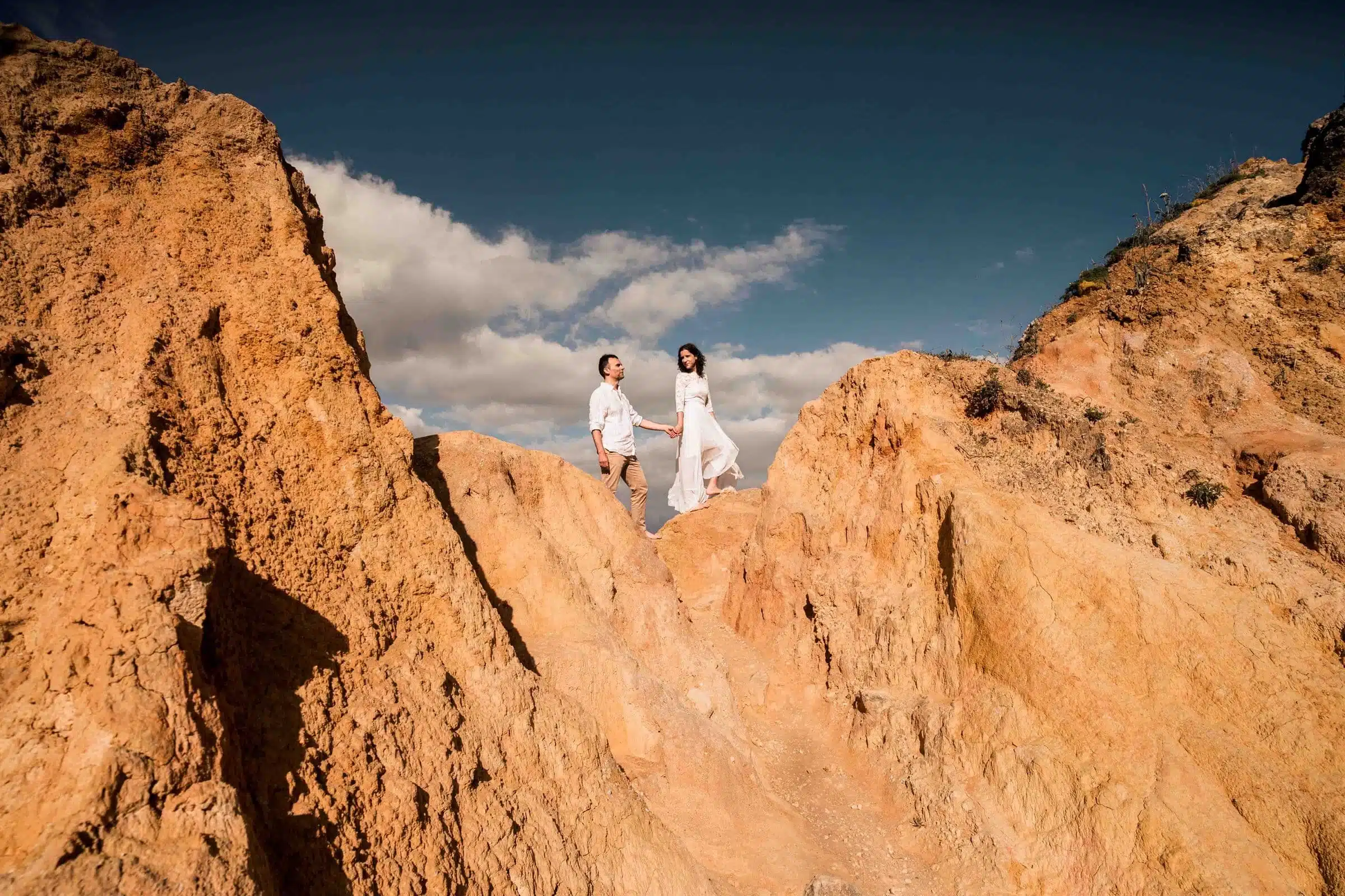 Accueil Couple de mariés main dans la main au sommet de falaises ocre, elopement photographié par Mégane Perrin